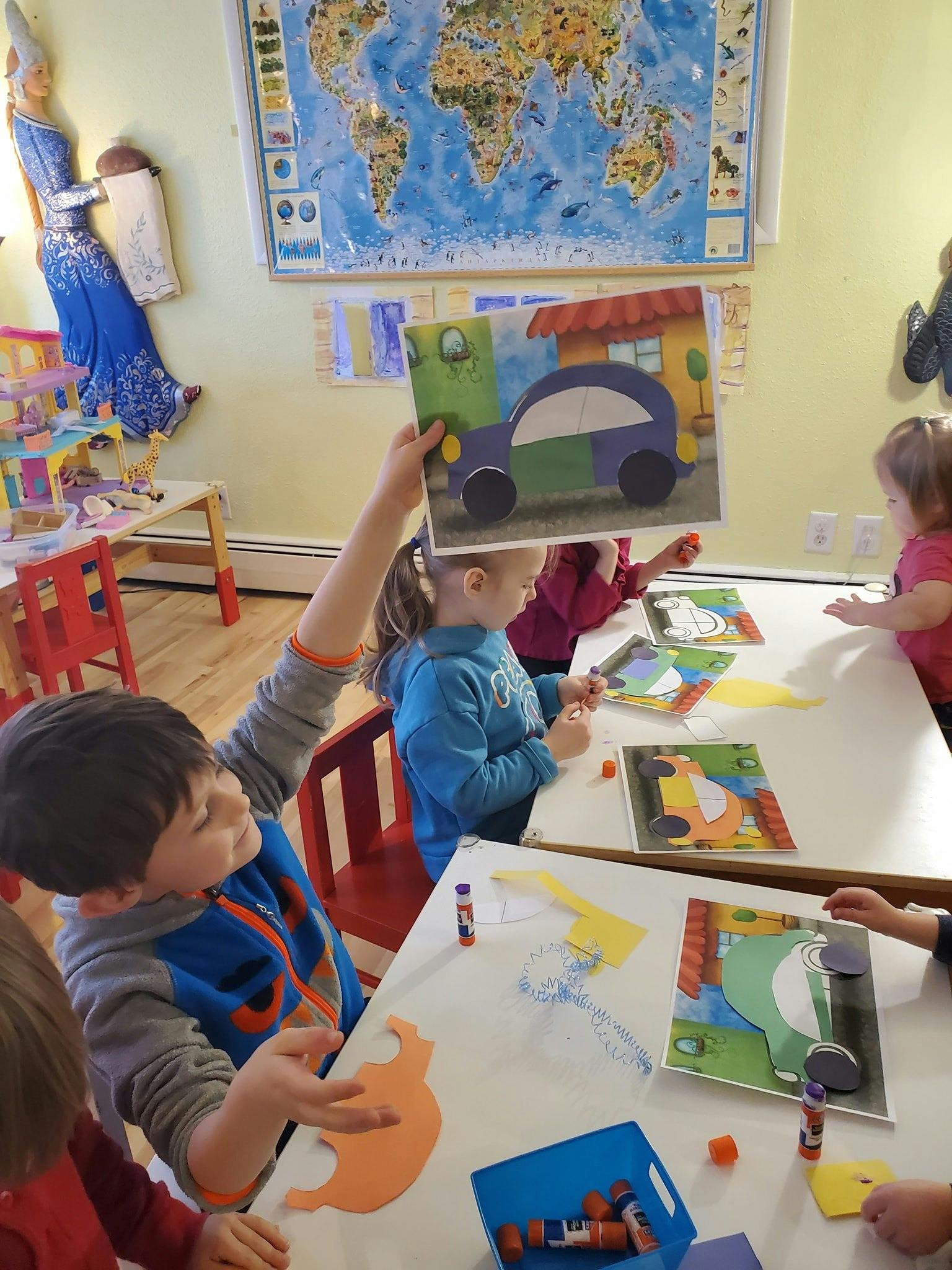 Person holding up a picture of a car in a classroom with children at tables