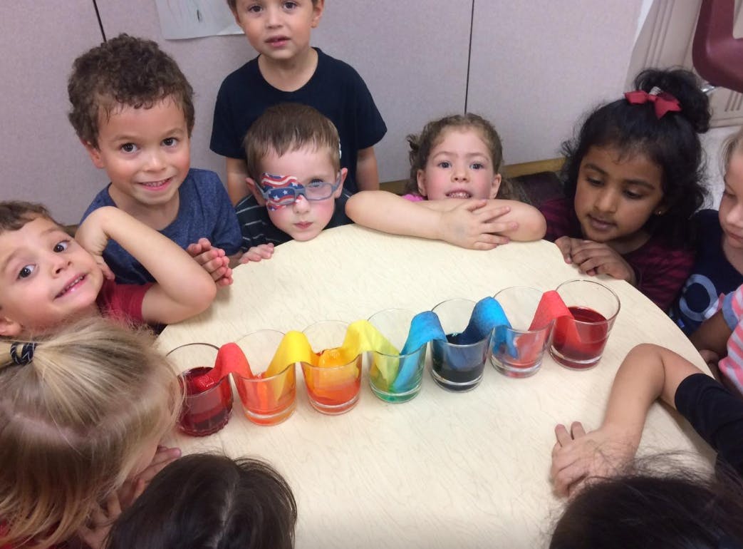 Children gathered around a table with colorful liquid in glasses