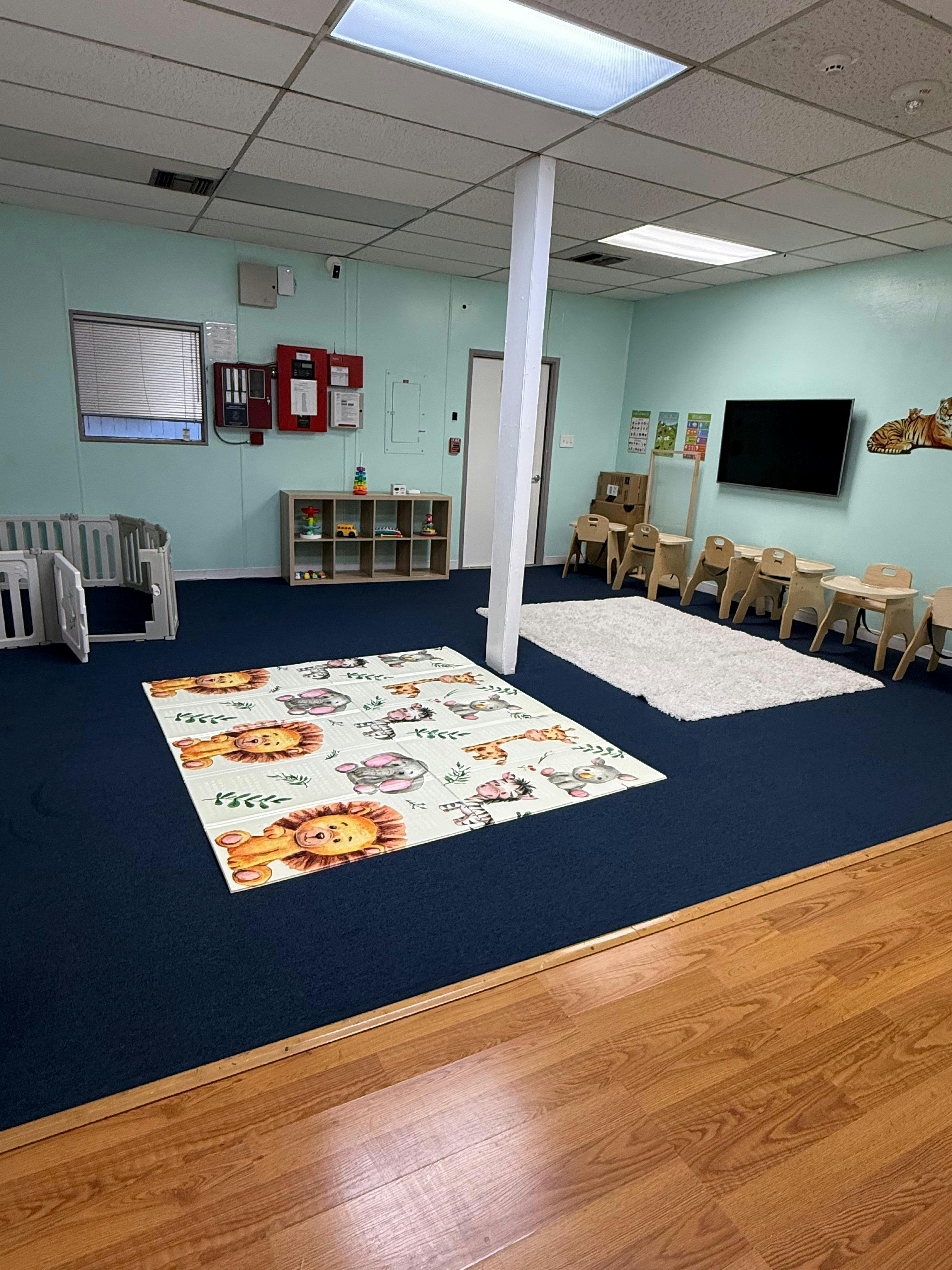 Empty children's playroom with small tables, playpen, and animal-themed playmat