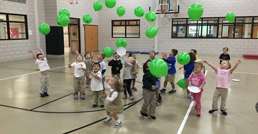 Children playing with green balloons in a gymnasium