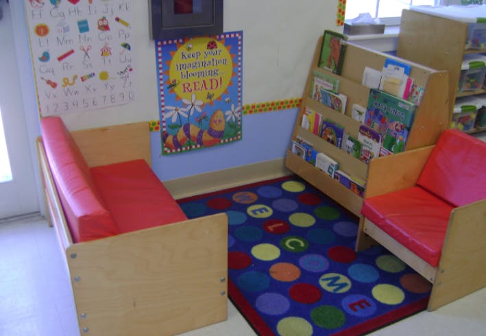 Classroom reading nook with small chairs, bookshelf, and alphabet rug
