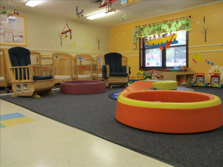 A childcare classroom with cribs, rocking chairs, and soft play equipment