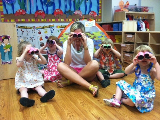 Person and three children sitting on floor looking through toy binoculars