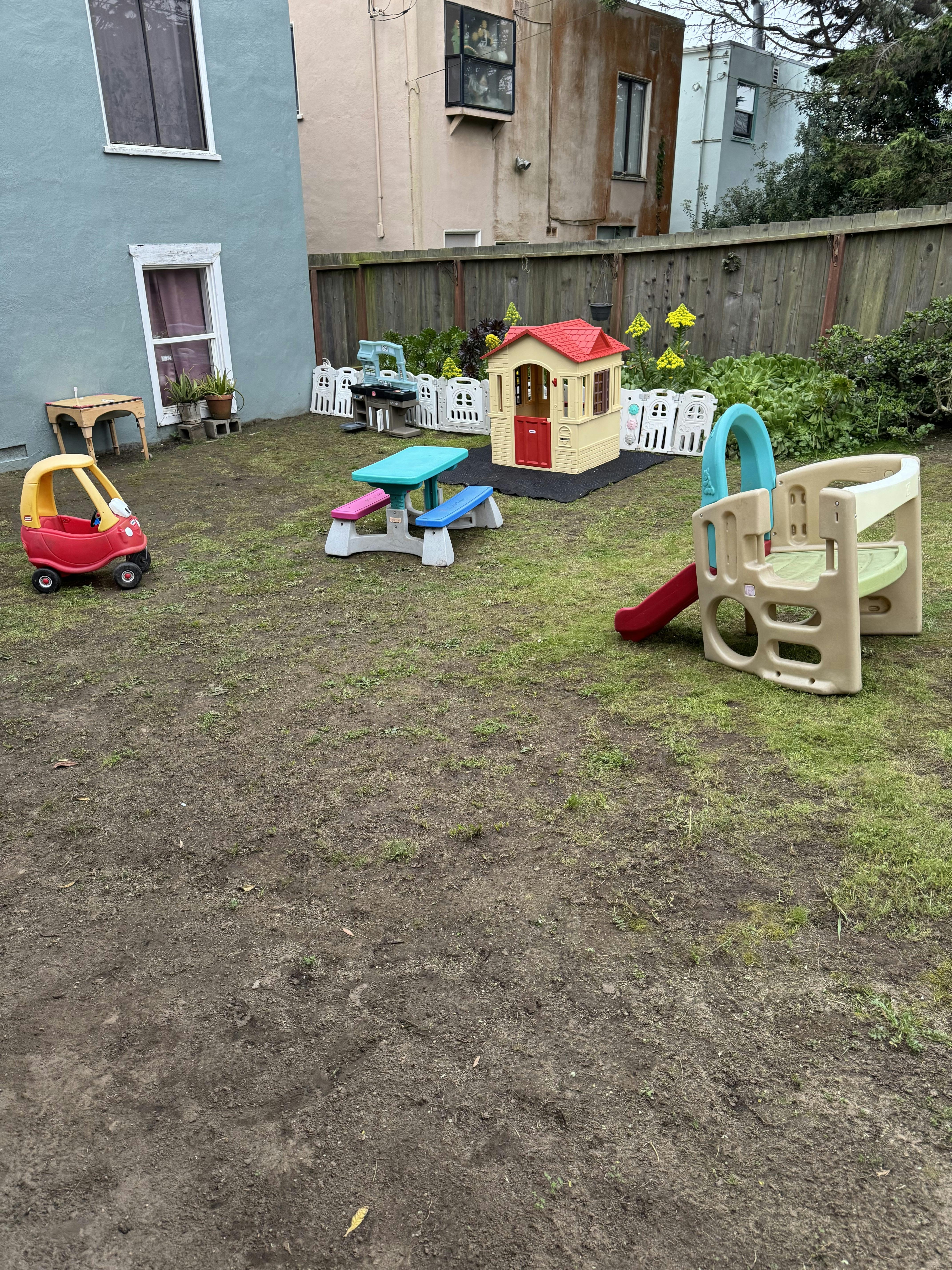 Children's play area with a red toy car, playhouse, and slide on grass and dirt