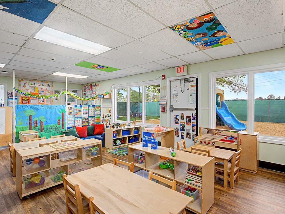 Empty preschool classroom with small tables, chairs, and learning materials