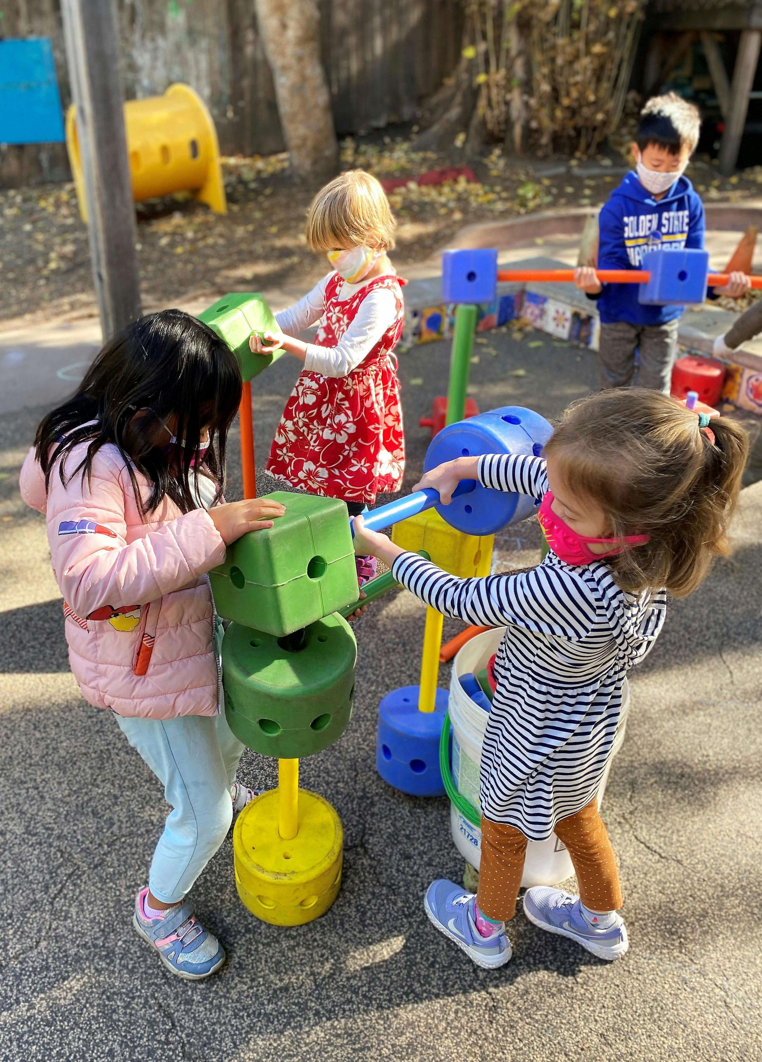 Three children playing with large colorful building blocks outdoors