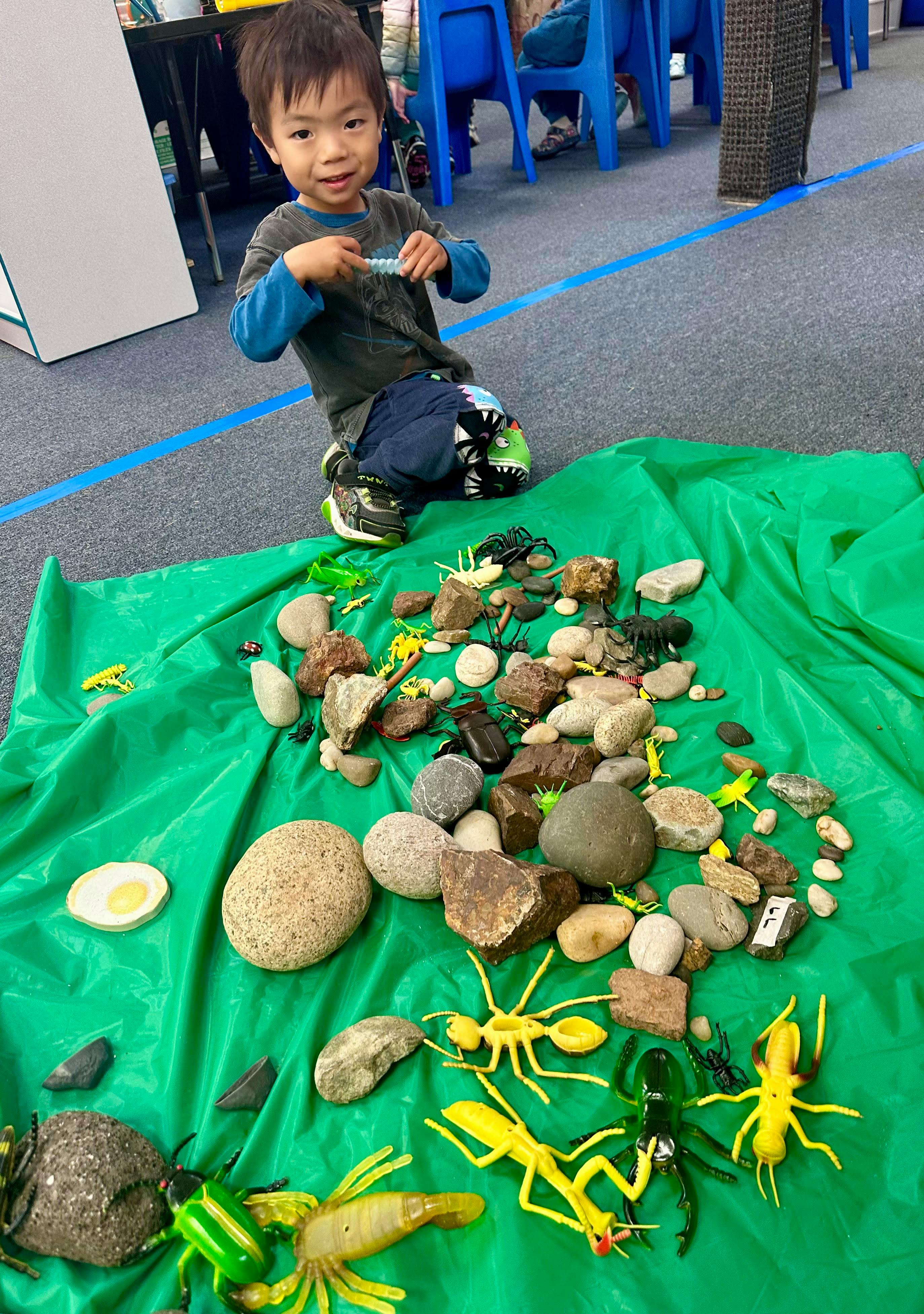 Child playing with plastic insect toys and rocks on a green mat