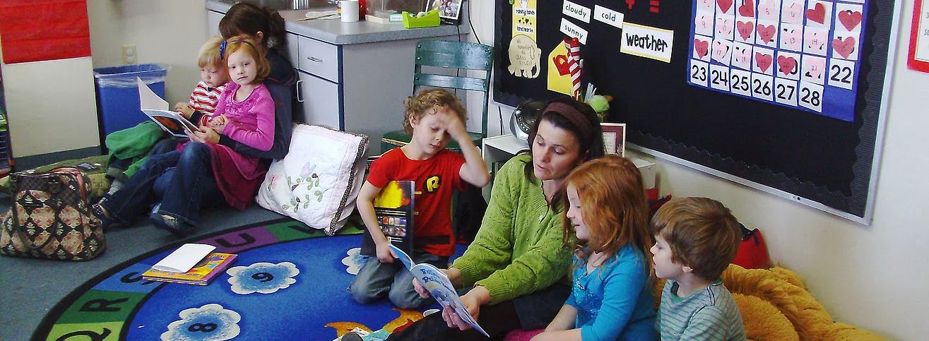 Adult and children sitting on floor reading books in a classroom