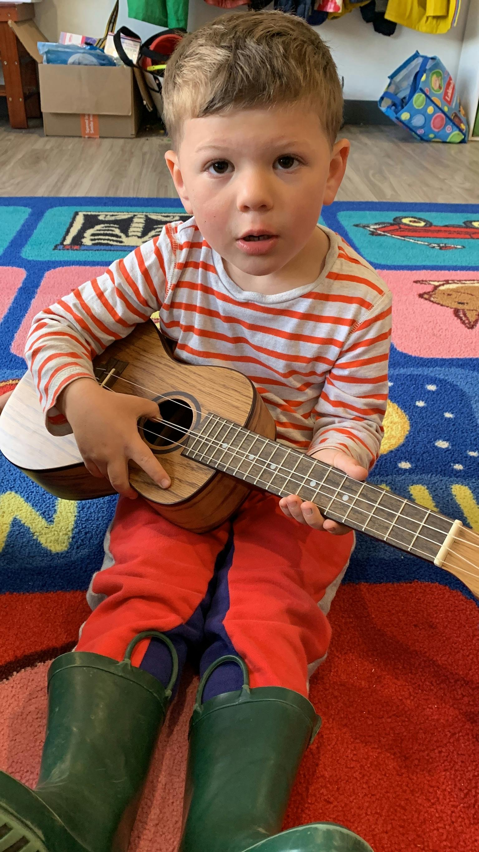 Child in striped shirt and boots holding a ukulele