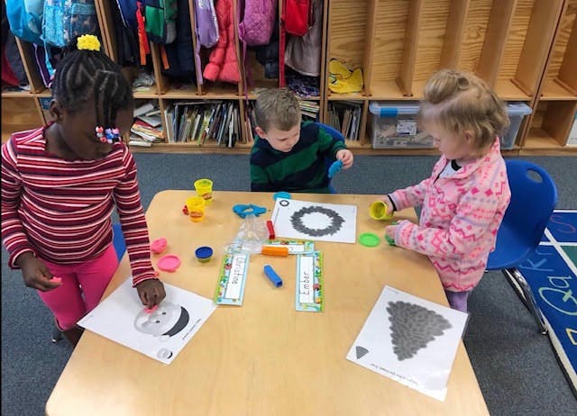 Three children playing with playdough at a table in a classroom