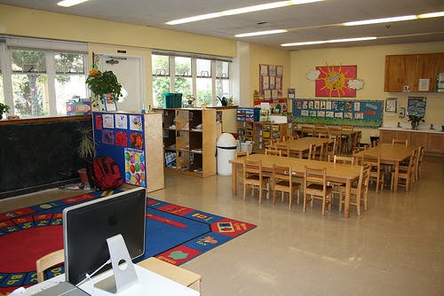 Classroom with small tables and chairs, a computer, and windows