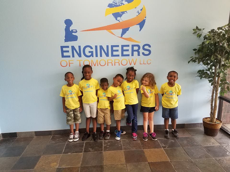 Group of children standing in front of a wall with "Engineers of Tomorrow" text