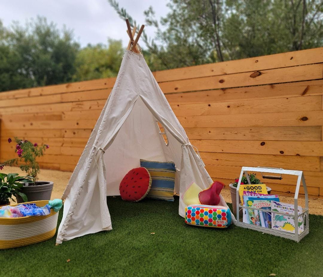 Play teepee on artificial grass with pillows, basket, and book caddy