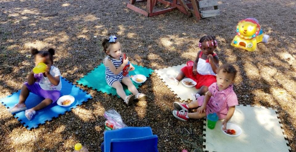 Four children sitting on mats outdoors with bowls