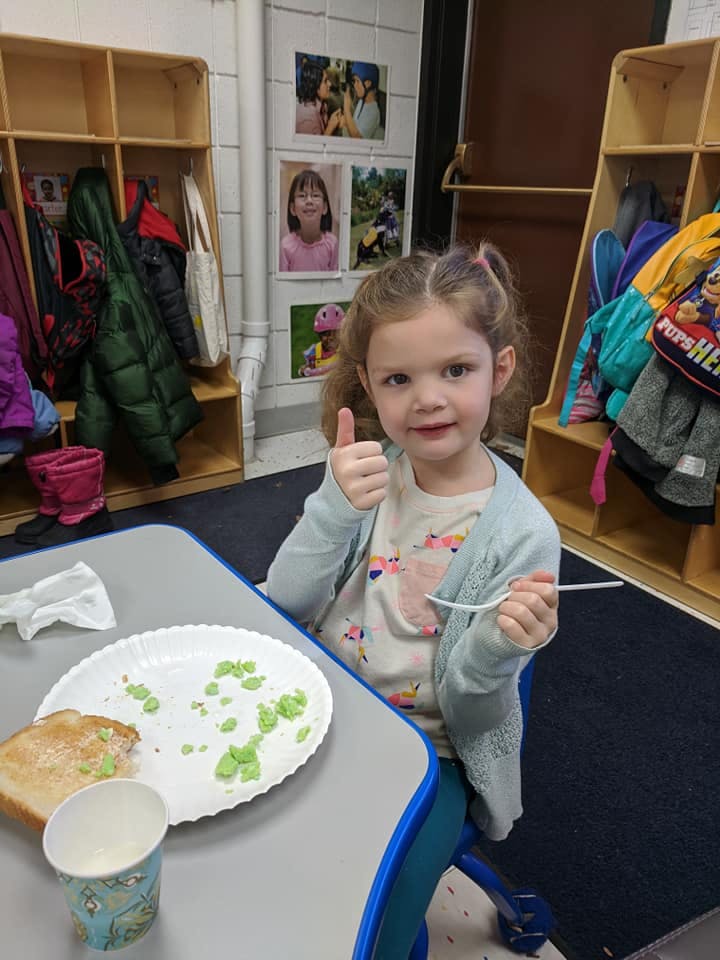 Child sitting at a table with a plate of food, giving a thumbs up