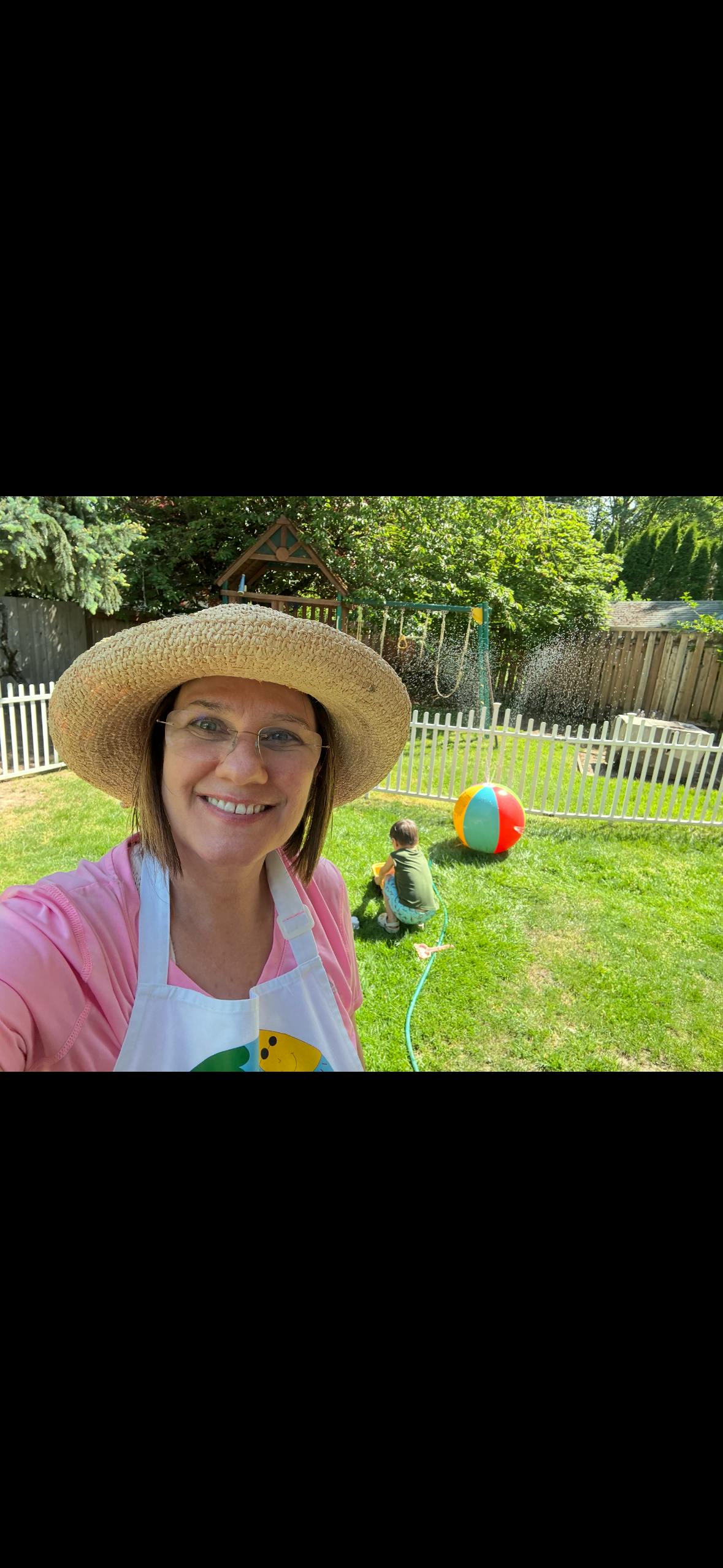 Person wearing a straw hat taking a selfie in a backyard with a child