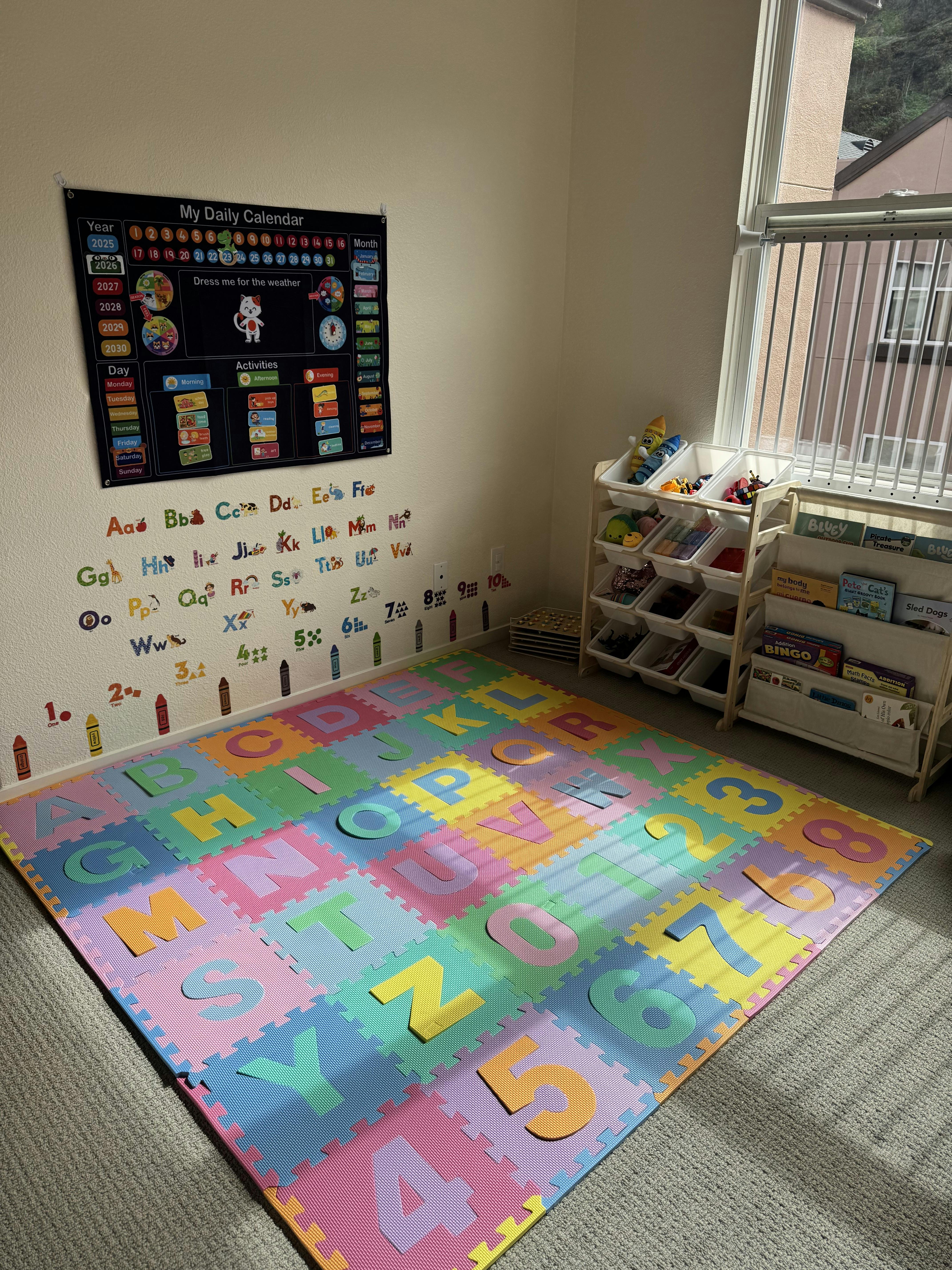 A playroom with an alphabet mat on the floor, calendar on the wall, and toy shelves