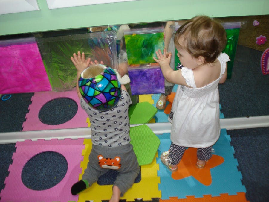 Two children playing with colorful sensory bags on a mirror