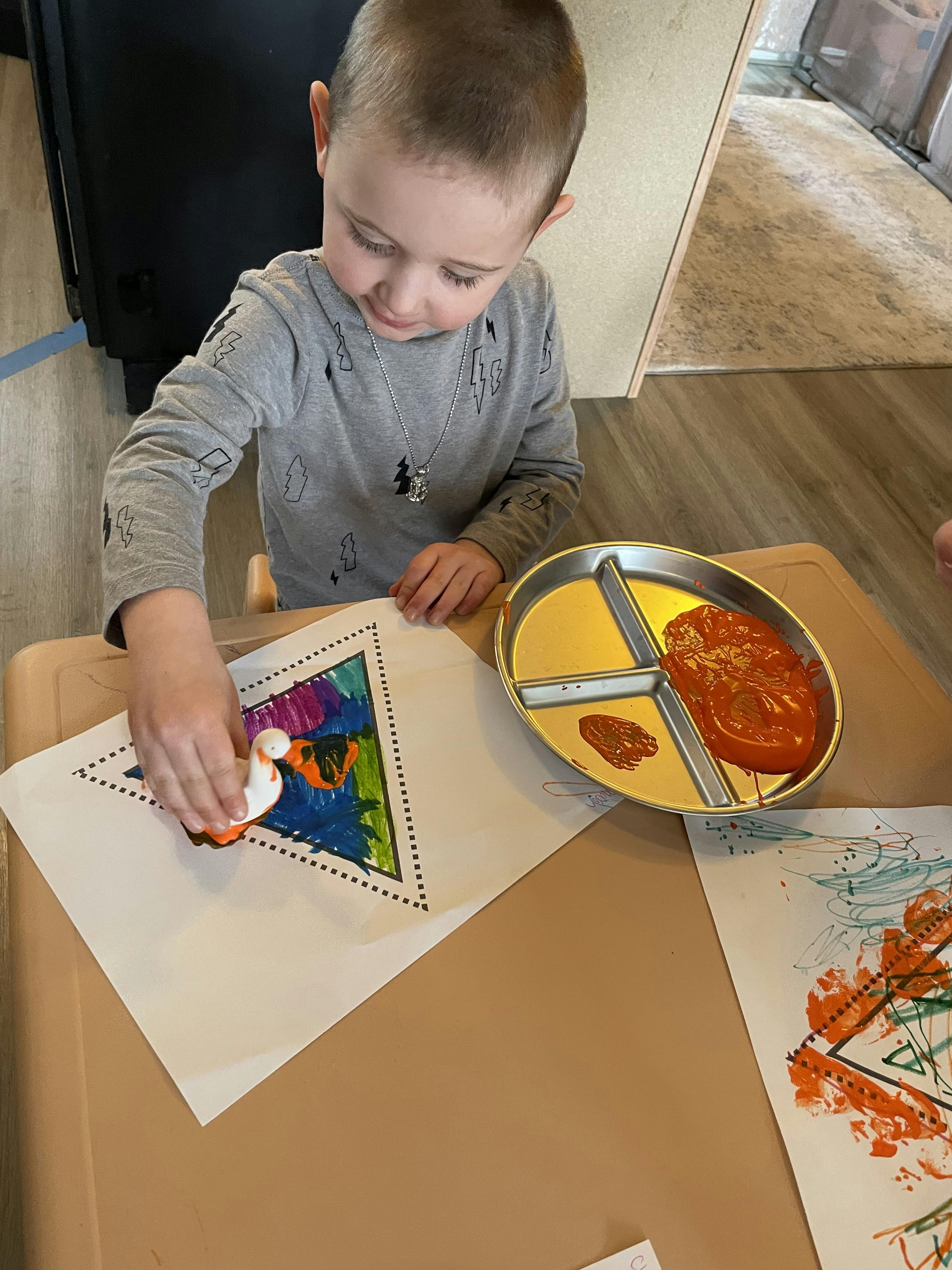 Child stamping paint onto a drawing with a duck-shaped stamper
