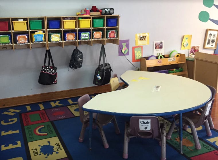 Classroom with a crescent-shaped table and chairs, storage cubbies, and bags