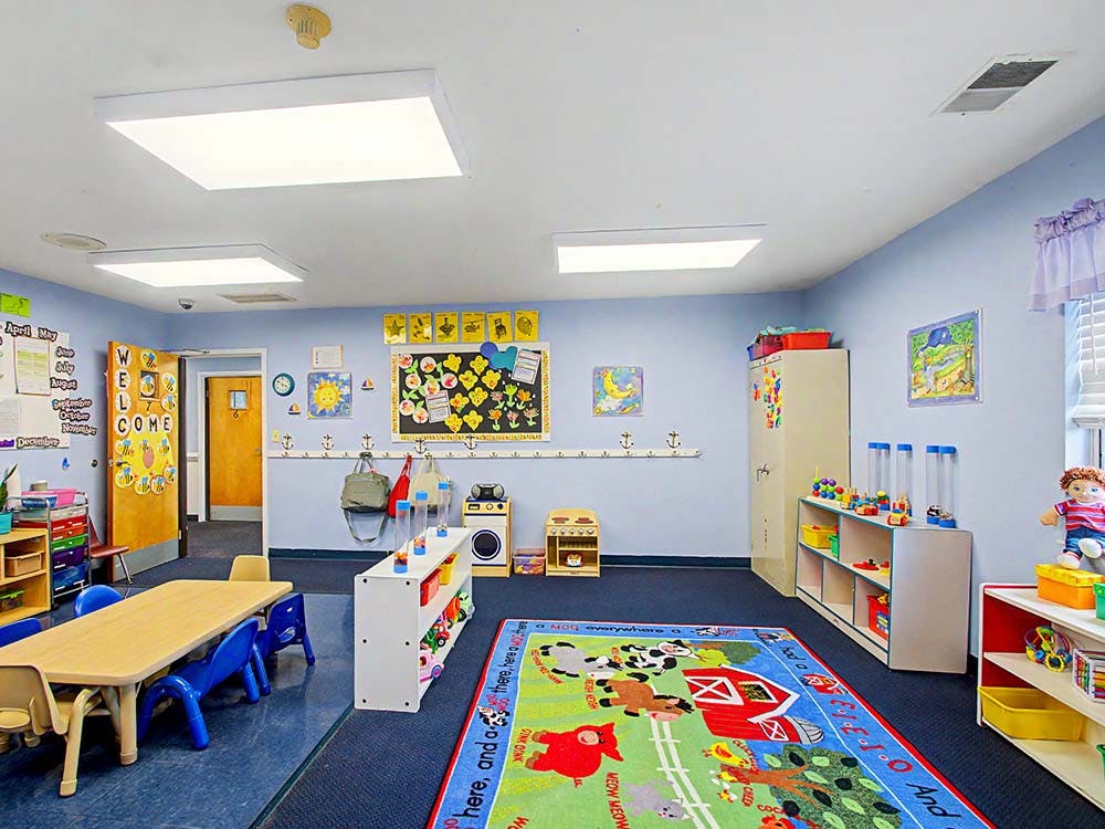 A classroom with a small table and chairs, a play rug, and shelves