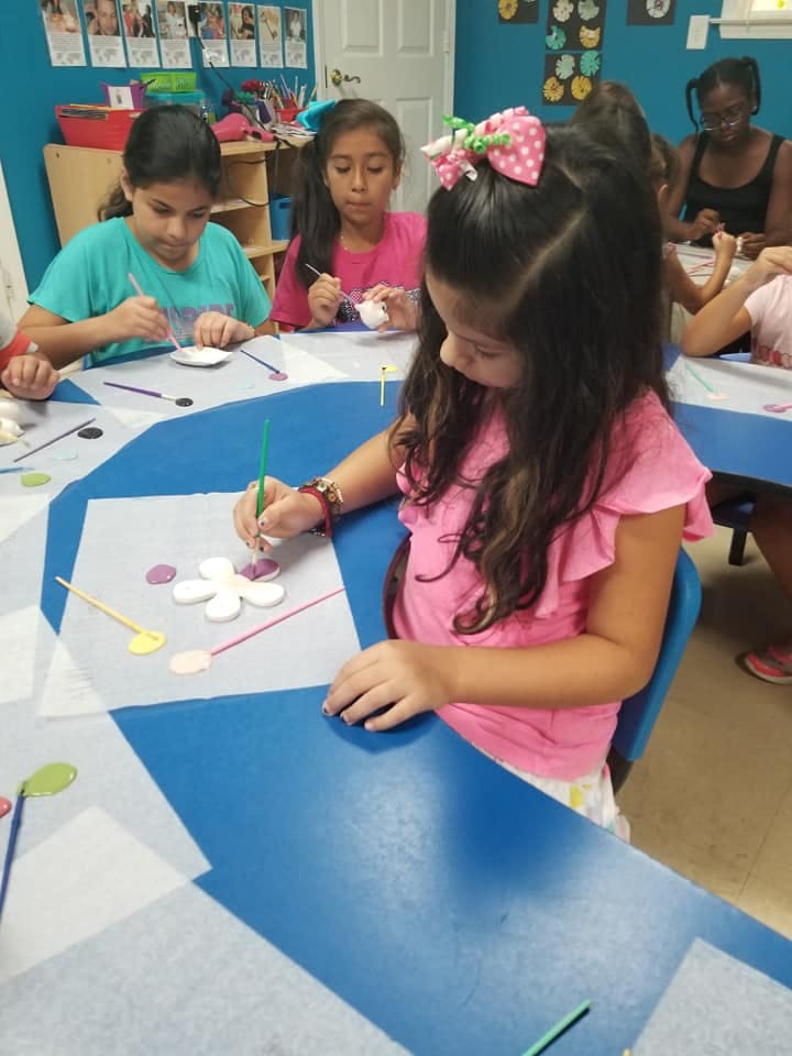 Child painting a flower shape at a table with other children