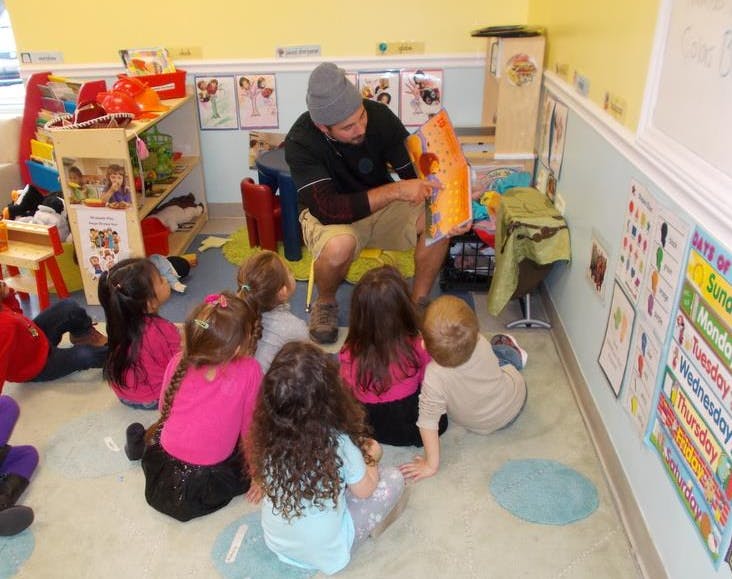 Person reading a book to a group of children in a classroom