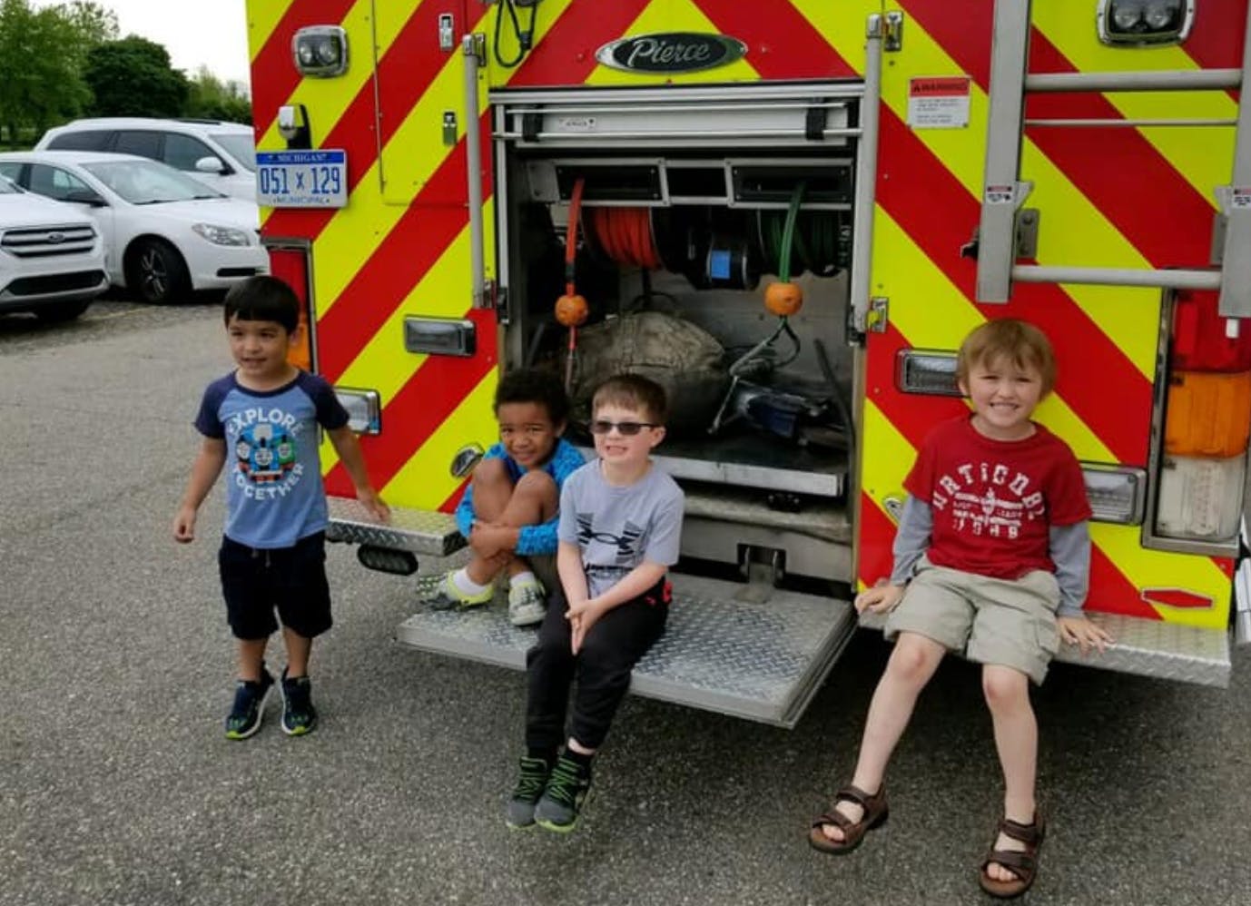Four children standing and sitting near the back of a fire truck