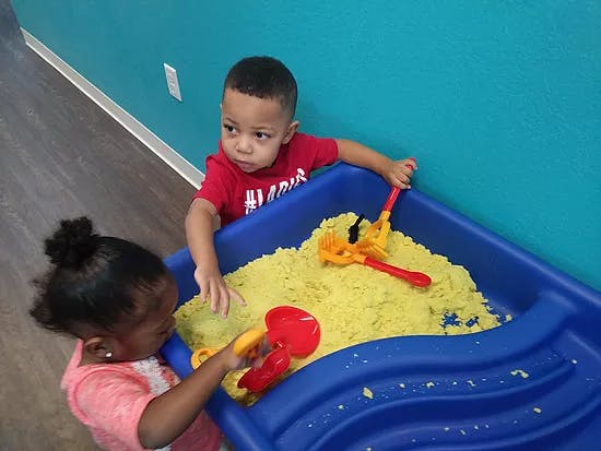 Two children playing with kinetic sand in a blue bin