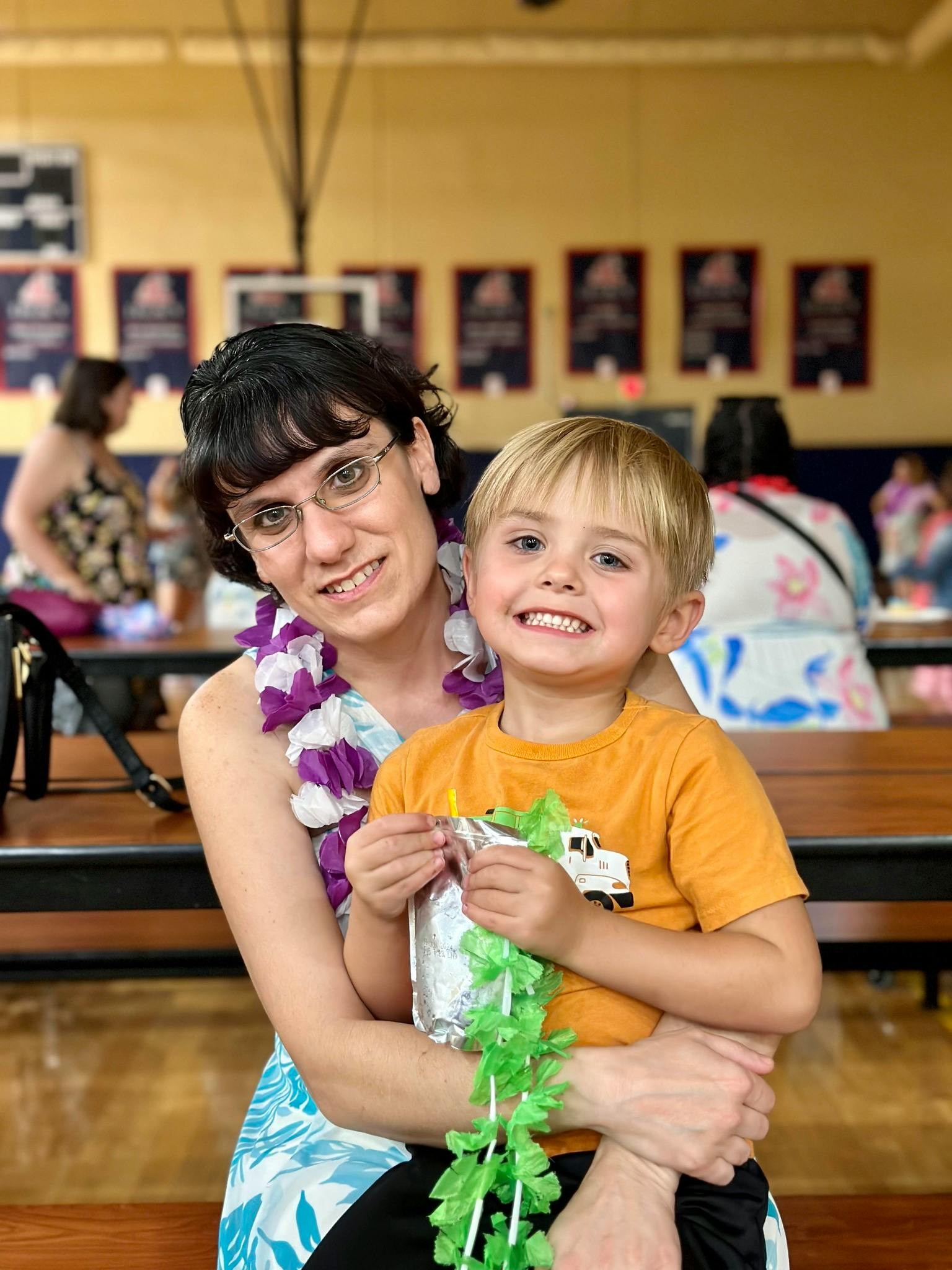 Person wearing a lei holding a child who is holding a green lei