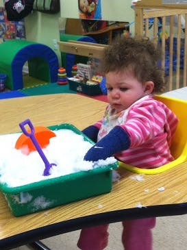 Child playing with snow in a green tray with a shovel and toy