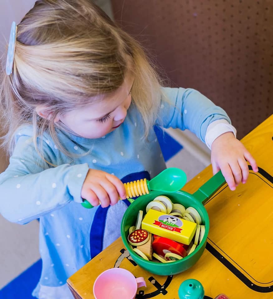 Child playing with toy food in a green pan