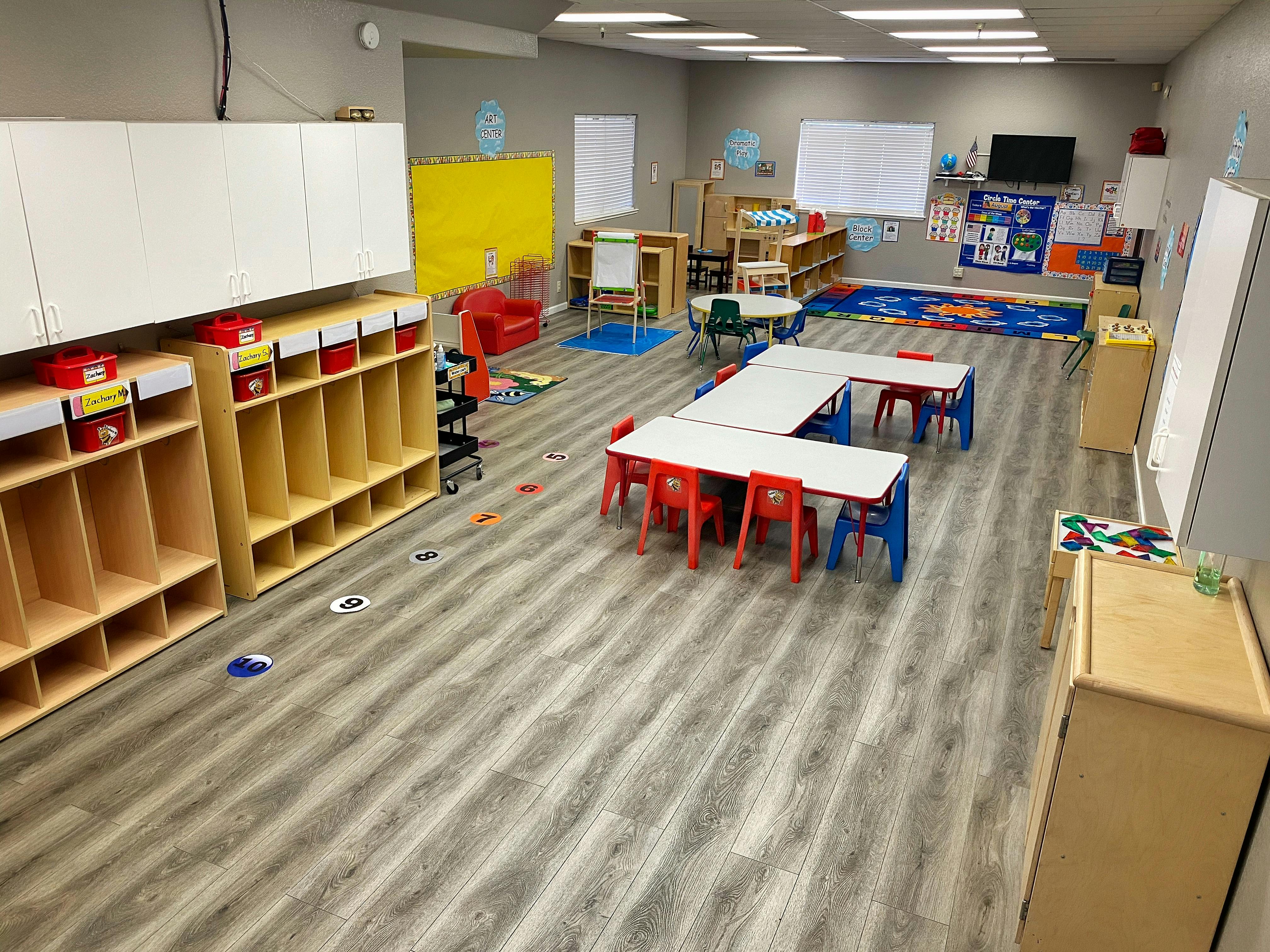 Empty classroom with small tables and chairs, storage cubbies, and a rug