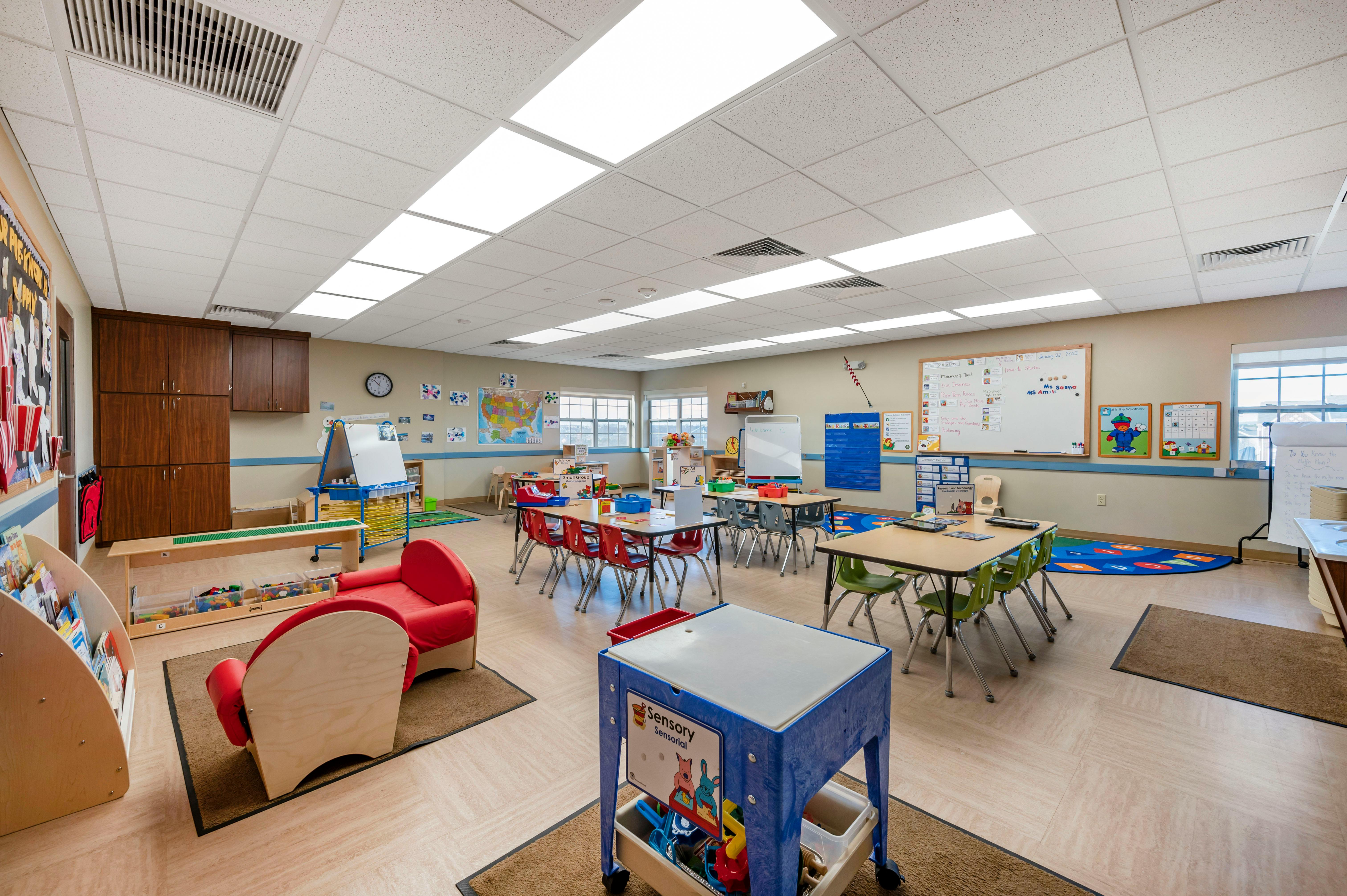 A colorful and brightly lit classroom with small tables and chairs, a play area, and whiteboards