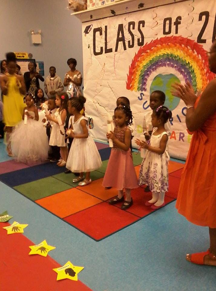 Children in dresses holding candles in front of a banner that says "CLASS of"