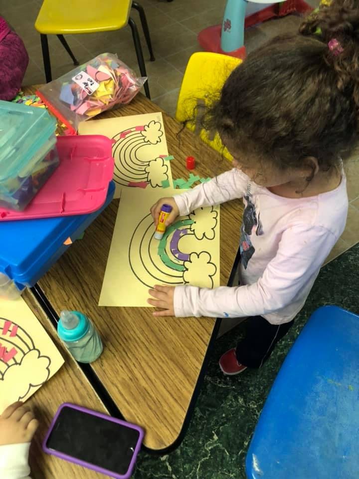 Child coloring a rainbow drawing at a table