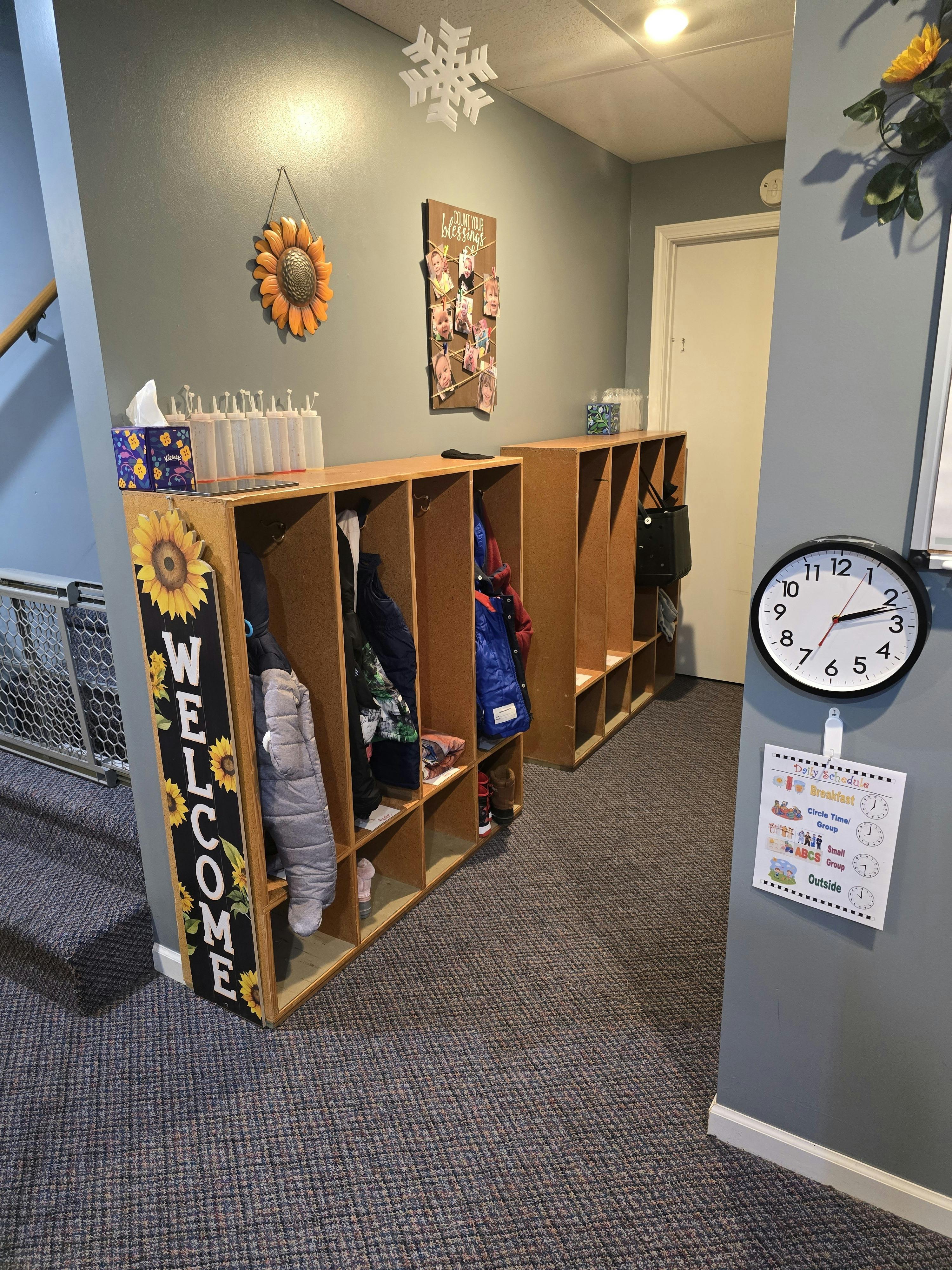 Children's cubbies with coats and boots, next to a daily schedule and clock