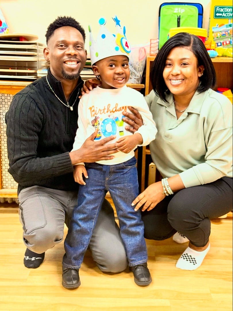 Two adults crouching beside a child wearing a birthday crown