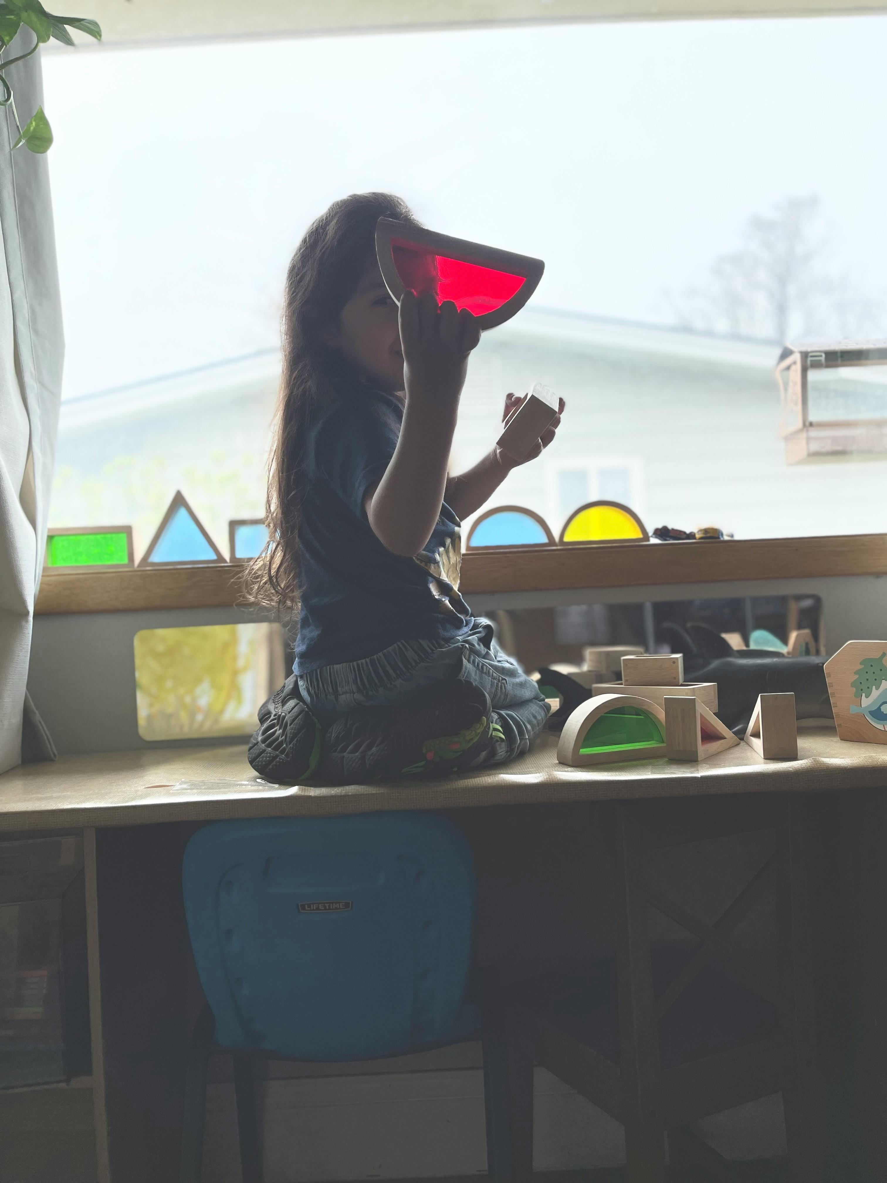 Child holding a red translucent block up to a window