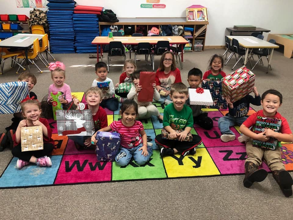 Group of children and adults sitting on a colorful alphabet rug with gifts