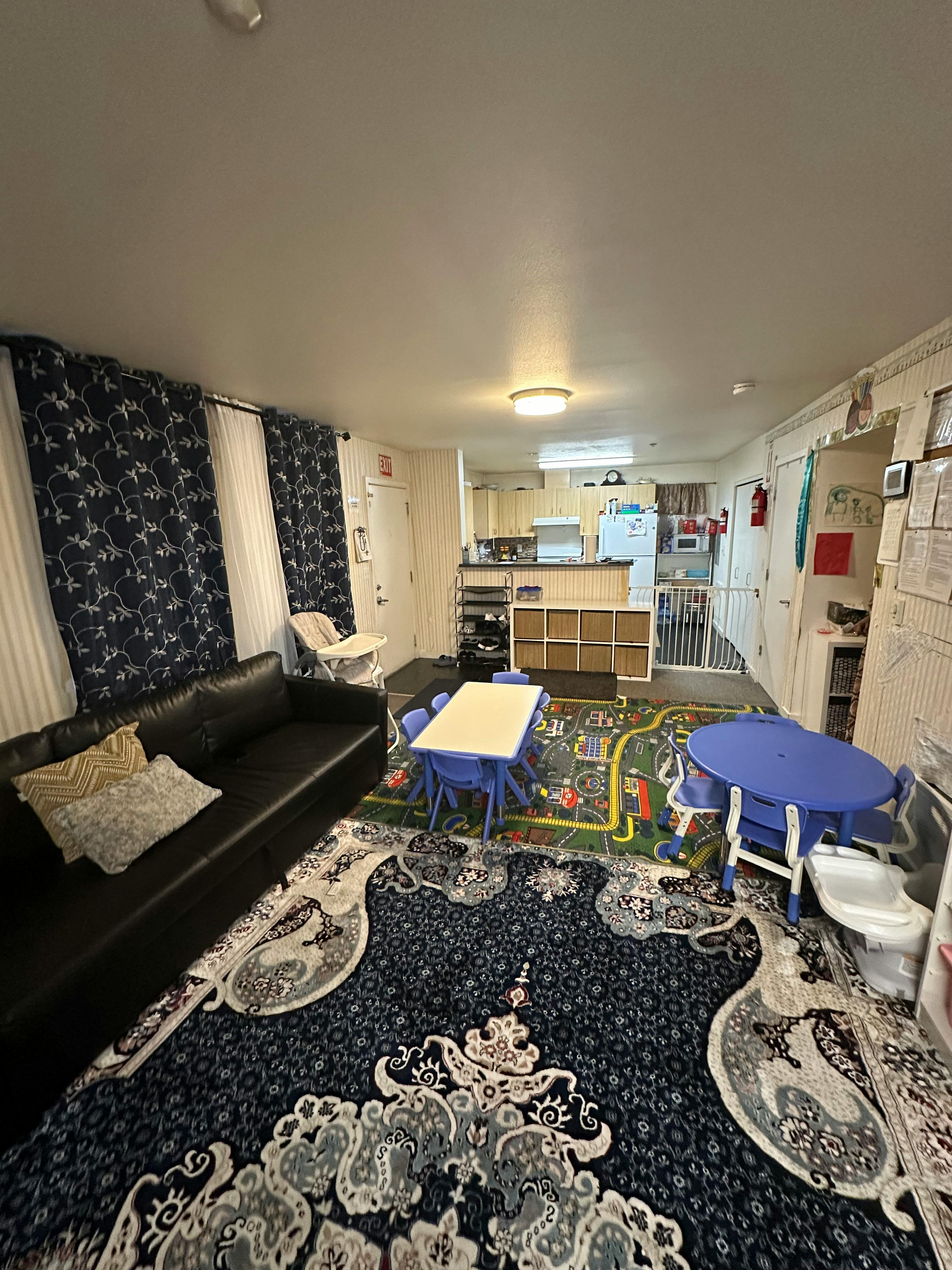 Living room with a black sofa, blue patterned curtains, and children's tables