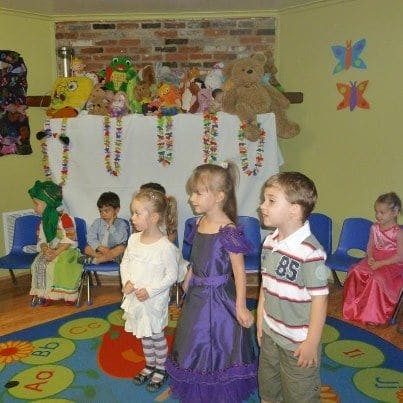 Children standing and sitting in a room with stuffed animals