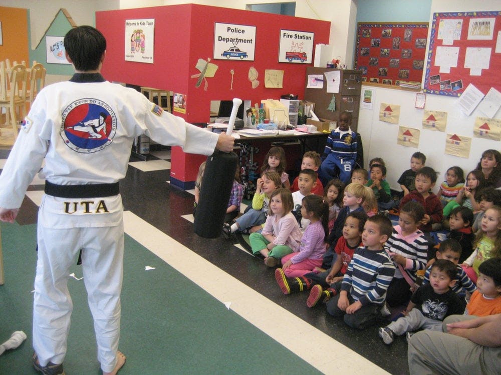 Person in martial arts uniform facing a group of children sitting on the floor