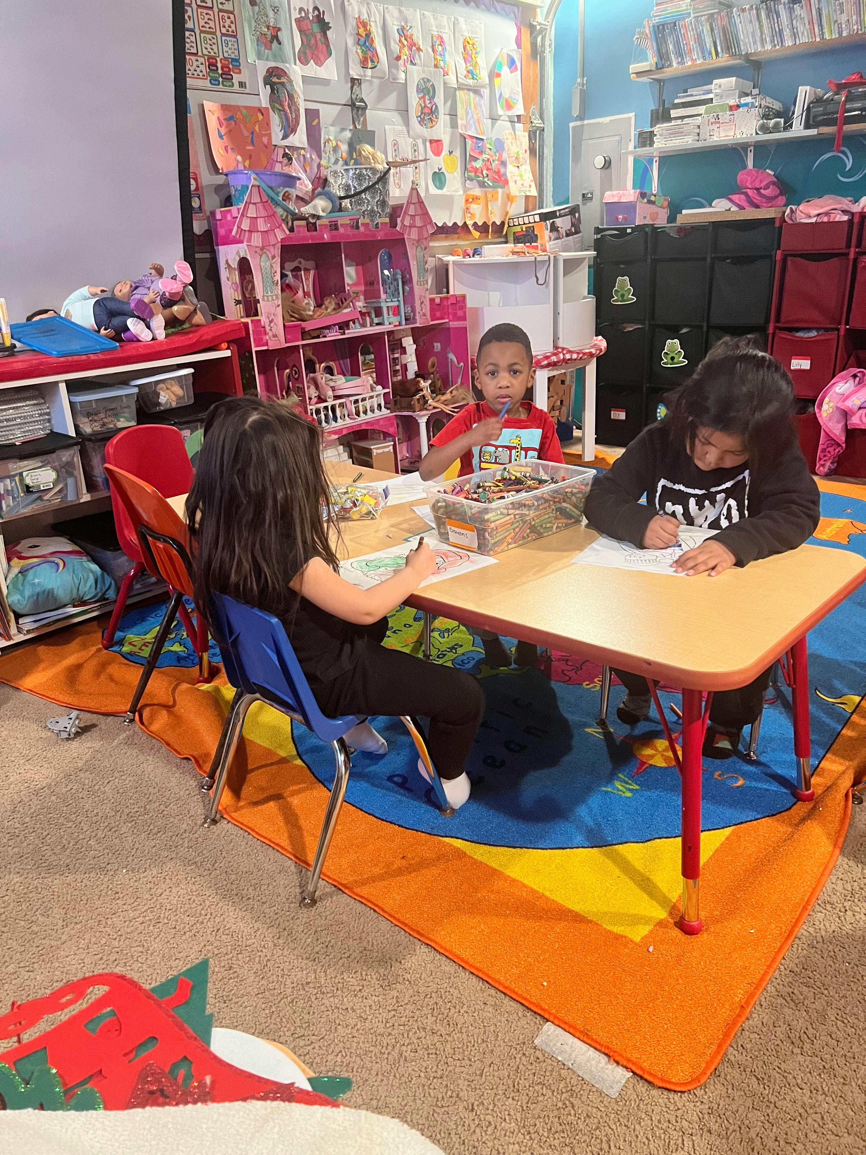 Three children sitting at a table drawing and playing