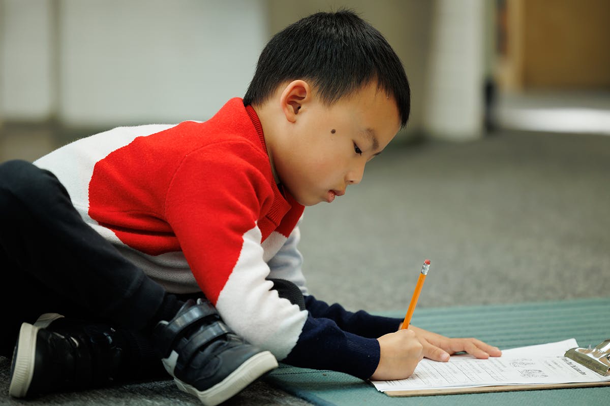 Child writing on paper with a pencil
