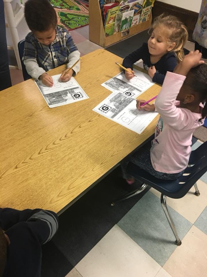Three children drawing at a table in a classroom