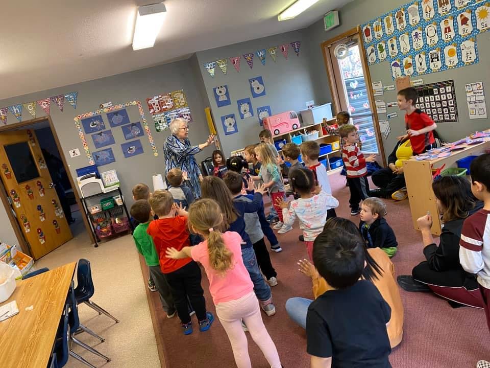 Adult leading a line of children in a classroom