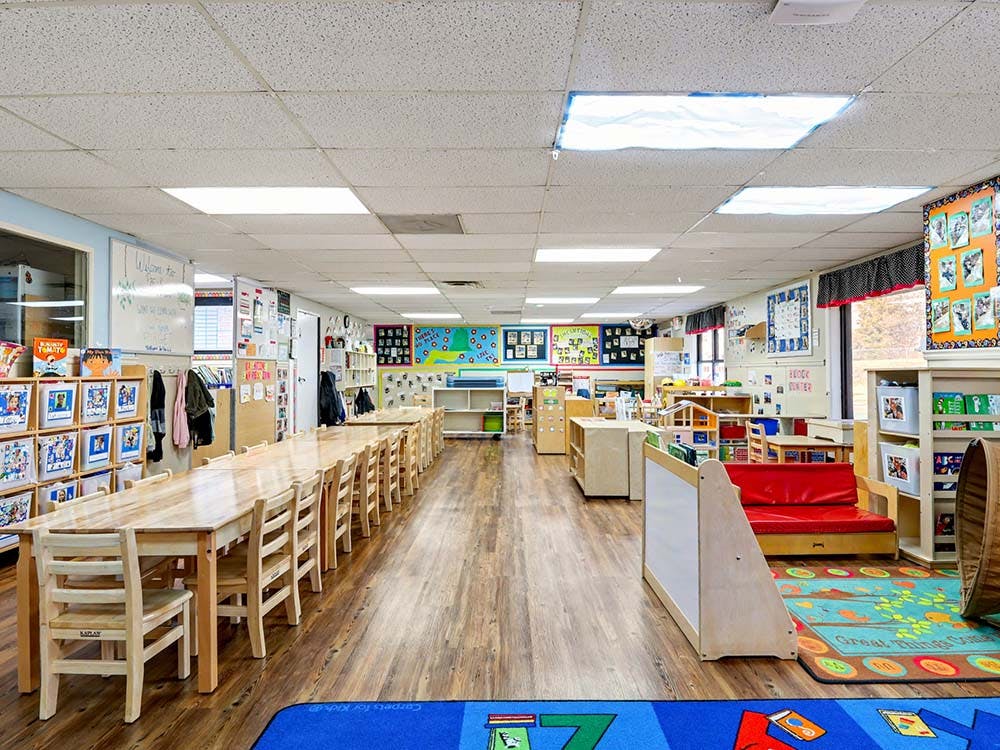 Classroom with long wooden tables and chairs, shelves, and colorful rugs