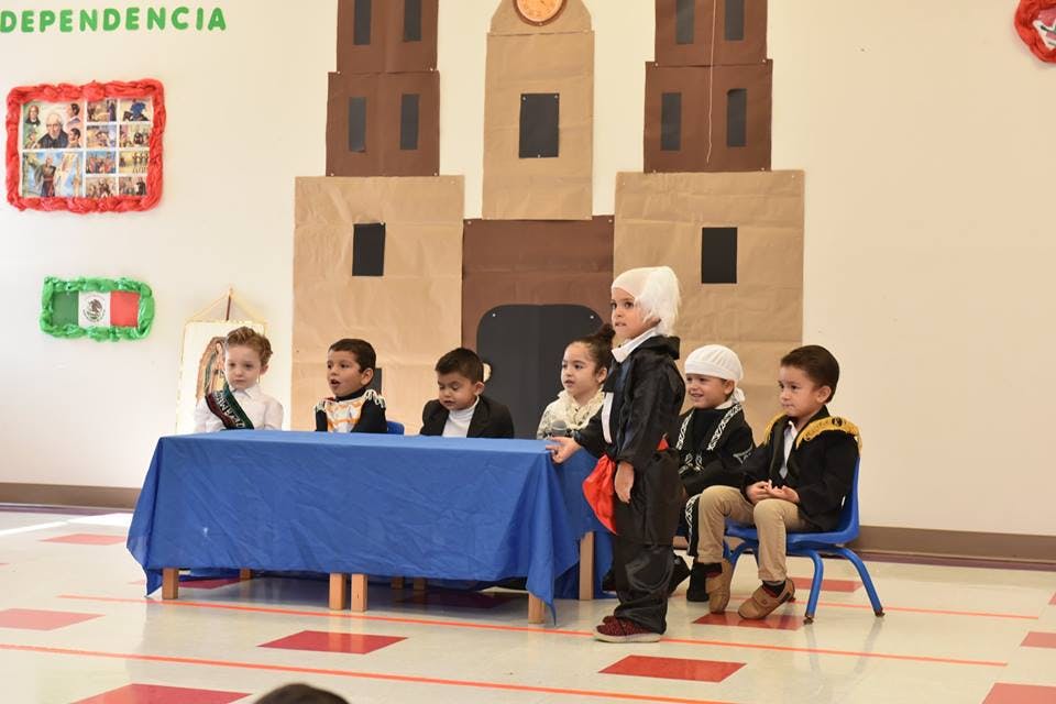 Children in costumes sitting and standing behind a blue table