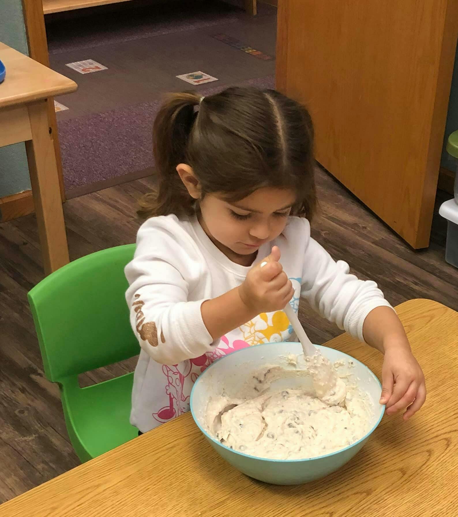 Child mixing ingredients in a bowl at a table